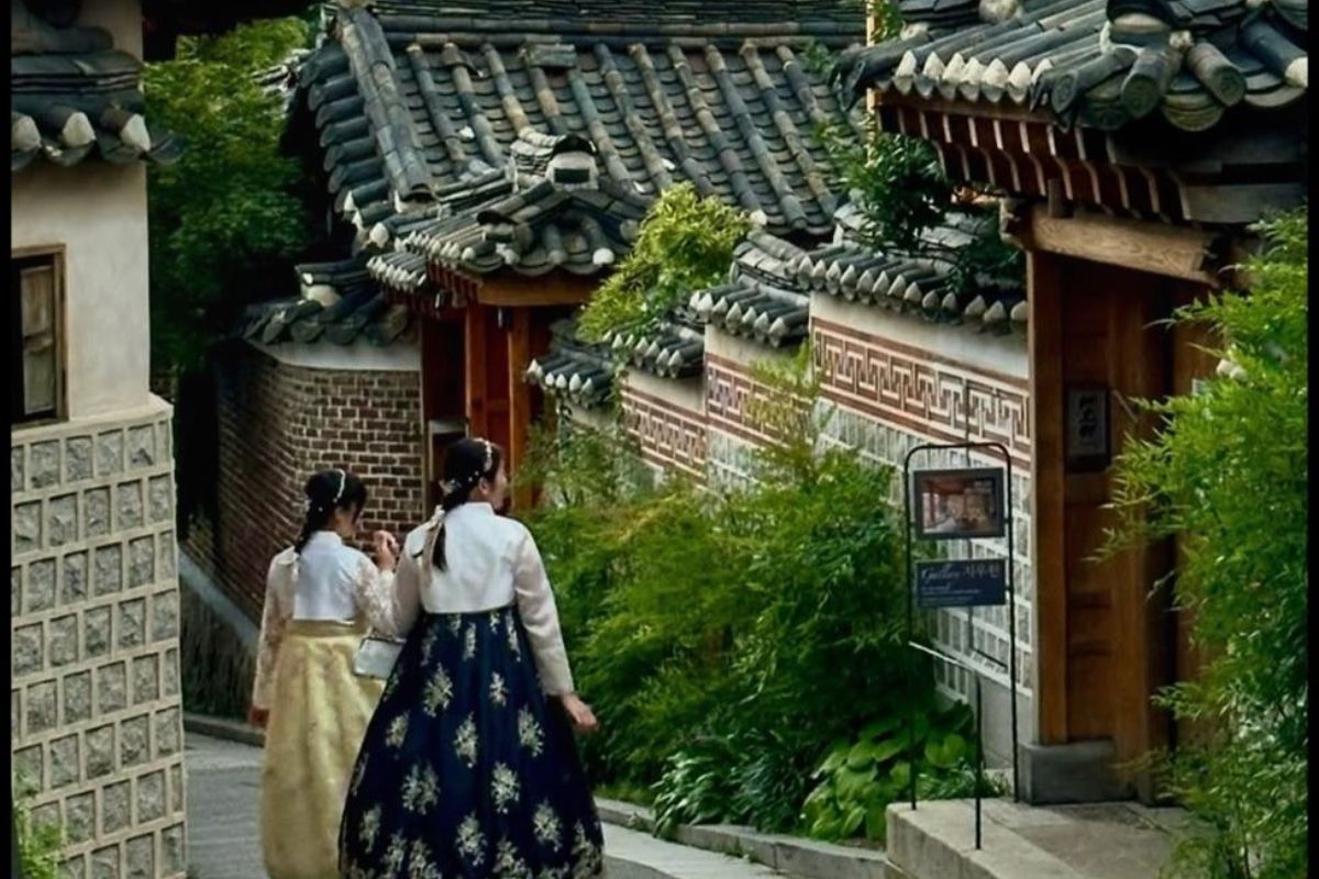 Women in traditional hanbok dress walk the lanes of Bukchon, with N Seoul Tower rising behind  